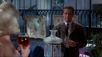 Movie still from “A New Kind of Love” (1963), directed by Melville Shavelson – A man in a suit and tie standing next to a vase; Medium shot, Over the shoulder angle