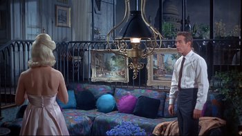 Movie still from “A New Kind of Love” (1963), directed by Melville Shavelson – A man and a woman are standing in a living room; Wide shot, Low angle