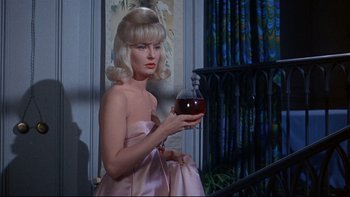 Movie still from “A New Kind of Love” (1963), directed by Melville Shavelson – A woman holding a glass of wine while sitting on a chair; Medium shot, Low angle