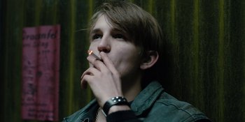 Movie still from “Dark” (2017), created by Baran bo Odar – A young man smoking a cigarette in front of a green curtain; Close Up shot, Low angle