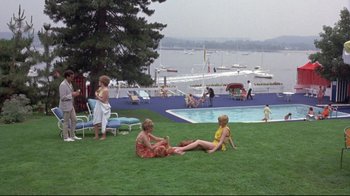 Movie still from “A New Leaf” (1971), directed by Elaine May – Two women and a child sitting on the grass near a pool; Extreme Wide shot, High angle