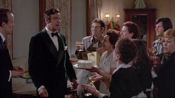 Movie still from “A New Leaf” (1971), directed by Elaine May – A group of people gathered around a cake in a living room; Medium shot, Over the shoulder angle