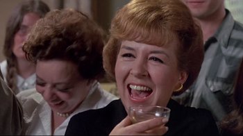 Movie still from “A New Leaf” (1971), directed by Elaine May – A woman laughing while holding a glass of water; Close Up shot, Over the shoulder angle