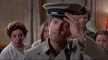 Movie still from “A New Leaf” (1971), directed by Elaine May – A man wearing a hat is saluting in front of a group of people; Close Up shot, Low angle