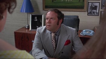 Movie still from “A New Leaf” (1971), directed by Elaine May – A man sitting at a desk wearing a suit and tie; Medium shot, Over the shoulder angle