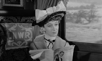 Movie still from “A Night to Remember” (1958), directed by Roy Ward Baker – A woman sitting on a train reading a magazine; Close Up shot, Over the shoulder angle