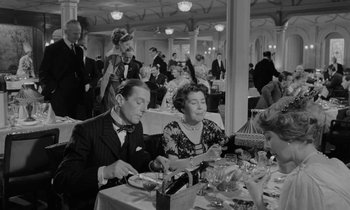 Movie still from “A Night to Remember” (1958), directed by Roy Ward Baker – A black and white photo of people sitting at a table; Medium shot, High angle