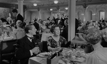 Movie still from “A Night to Remember” (1958), directed by Roy Ward Baker – An old black and white photo of people sitting at a table; Medium shot, High angle