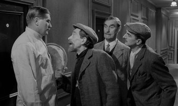 Movie still from “A Night to Remember” (1958), directed by Roy Ward Baker – A group of men standing next to each other in a room; Medium shot, Over the shoulder angle