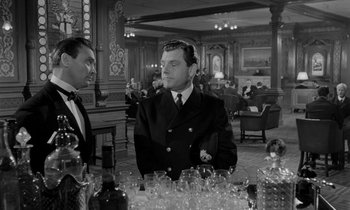 Movie still from “A Night to Remember” (1958), directed by Roy Ward Baker – A man in a suit and tie in front of a bunch of empty glasses; Medium shot, Over the shoulder angle