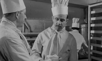Movie still from “A Night to Remember” (1958), directed by Roy Ward Baker – Two men wearing chef's hats in an industrial kitchen; Medium shot, Low angle