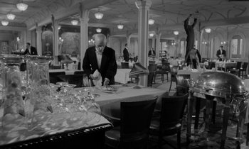 Movie still from “A Night to Remember” (1958), directed by Roy Ward Baker – A man standing at a table in a restaurant; Wide shot, Low angle