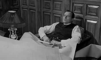 Movie still from “A Night to Remember” (1958), directed by Roy Ward Baker – A man sitting at a table with papers in front of him; Medium shot, High angle