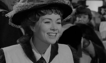 Movie still from “A Night to Remember” (1958), directed by Roy Ward Baker – A woman wearing a hat and smiling for the camera; Close Up shot, Over the shoulder angle