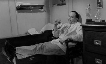Movie still from “A Night to Remember” (1958), directed by Roy Ward Baker – A black and white photo of a man sitting in a chair; Medium shot, High angle