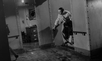 Movie still from “A Night to Remember” (1958), directed by Roy Ward Baker – A black and white photo of a man leaning against a wall; Wide shot, High angle