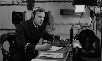 Movie still from “A Night to Remember” (1958), directed by Roy Ward Baker – A man wearing headphones and sitting in front of a computer; Medium shot, High angle