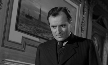 Movie still from “A Night to Remember” (1958), directed by Roy Ward Baker – A man wearing a suit and tie standing in front of a painting; Close Up shot, Low angle