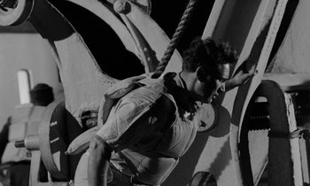 Movie still from “A Night to Remember” (1958), directed by Roy Ward Baker – A man hanging from a rope on the side of a building; Medium shot, Low angle