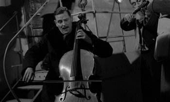 Movie still from “A Night to Remember” (1958), directed by Roy Ward Baker – A man holding a cello while another man plays the violin; Medium shot, Low angle