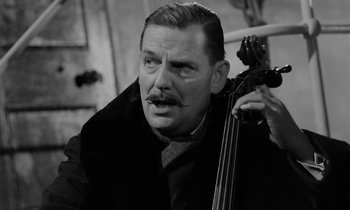 Movie still from “A Night to Remember” (1958), directed by Roy Ward Baker – A black and white photo of a man holding a cello; Close Up shot, Low angle