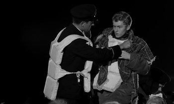 Movie still from “A Night to Remember” (1958), directed by Roy Ward Baker – A man is putting on a jacket by a police officer; Medium shot, High angle
