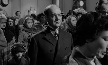 Movie still from “A Night to Remember” (1958), directed by Roy Ward Baker – A man in a suit and tie in front of a group of people; Medium shot, Over the shoulder angle