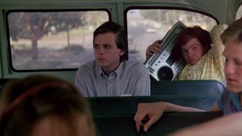 Movie still from “A Nightmare on Elm Street 2: Freddy's Revenge” (1985), directed by Jack Sholder – A man sitting on the back of a bus while holding a radio in his hand; Medium shot, Over the shoulder angle