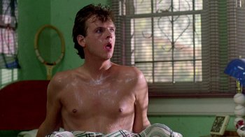 A shirtless man sitting on a bed in a room