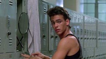 Movie still from “A Nightmare on Elm Street 2: Freddy's Revenge” (1985), directed by Jack Sholder – A young man in a black tank top looking at himself in a mirror; Medium shot, Low angle