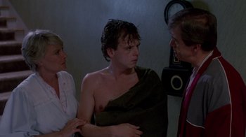 Movie still from “A Nightmare on Elm Street 2: Freddy's Revenge” (1985), directed by Jack Sholder – A man with a towel around his neck is talking to two other people; Medium shot, Over the shoulder angle