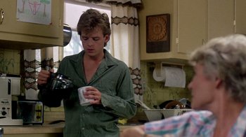 Movie still from “A Nightmare on Elm Street 2: Freddy's Revenge” (1985), directed by Jack Sholder – A man in a green shirt is holding a cup; Medium shot, Over the shoulder angle