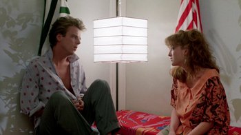 Movie still from “A Nightmare on Elm Street 2: Freddy's Revenge” (1985), directed by Jack Sholder – A man and a woman sitting on a bed in front of a lamp; Medium shot, Low angle