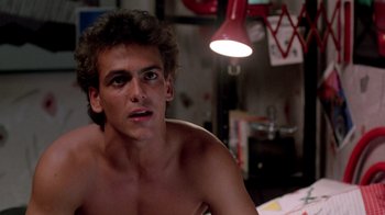 Movie still from “A Nightmare on Elm Street 2: Freddy's Revenge” (1985), directed by Jack Sholder – A shirtless man sitting in front of a lamp; Close Up shot, Low angle