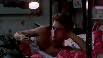 Movie still from “A Nightmare on Elm Street 2: Freddy's Revenge” (1985), directed by Jack Sholder – A man laying in a bed holding a remote control; Medium shot, Low angle