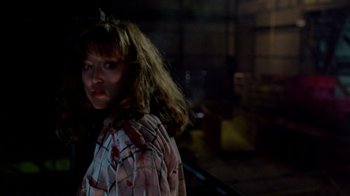 Movie still from “A Nightmare on Elm Street 2: Freddy's Revenge” (1985), directed by Jack Sholder – A woman in a pink and white shirt standing in a dark room; Close Up shot, Over the shoulder angle