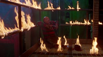 Movie still from “A Nightmare on Elm Street 2: Freddy's Revenge” (1985), directed by Jack Sholder – A man kneeling down in front of flames; Wide shot, High angle