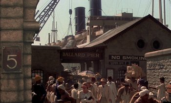 Movie still from “A Passage to India” (1984), directed by David Lean – A group of people standing outside of a building; Extreme Wide shot, High angle