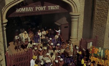 Movie still from “A Passage to India” (1984), directed by David Lean – A group of men in hats and uniforms standing in front of a building; Extreme Wide shot, High angle