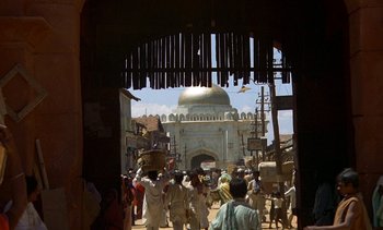 Movie still from “A Passage to India” (1984), directed by David Lean – A group of people walking down a street with a building in the background; Extreme Wide shot, Low angle