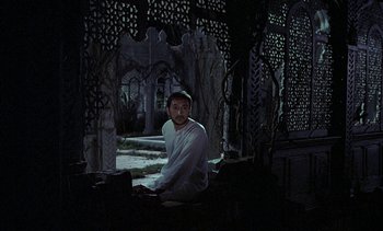 Movie still from “A Passage to India” (1984), directed by David Lean – A man sitting on a chair in a dark room; Wide shot, High angle