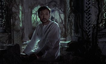 Movie still from “A Passage to India” (1984), directed by David Lean – A man in a white shirt is sitting in a dark room; Medium shot, Low angle