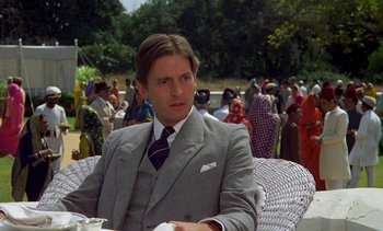 Movie still from “A Passage to India” (1984), directed by David Lean – A man in a suit and tie sitting in a chair; Medium shot, Low angle