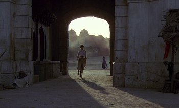 Movie still from “A Passage to India” (1984), directed by David Lean – A person riding a bike through a tunnel; Extreme Wide shot, Over the shoulder angle
