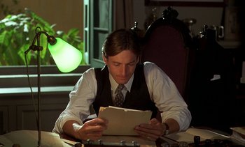 Movie still from “A Passage to India” (1984), directed by David Lean – A man sitting at a table reading a paper; Medium shot, Low angle