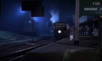 Movie still from “A Passage to India” (1984), directed by David Lean – A train on the tracks at night with smoke billowing out of it; Extreme Wide shot, High angle