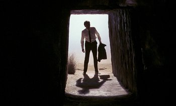 Movie still from “A Passage to India” (1984), directed by David Lean – A man standing in a tunnel with a suit and bag; Wide shot, Low angle