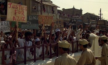 Movie still from “A Passage to India” (1984), directed by David Lean – A group of people standing next to each other holding signs; Wide shot, High angle