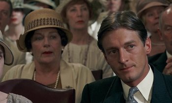 Movie still from “A Passage to India” (1984), directed by David Lean – A man and a woman are sitting next to each other in front of other people; Close Up shot, Over the shoulder angle