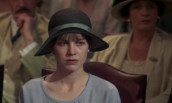 Movie still from “A Passage to India” (1984), directed by David Lean – A woman wearing a black hat sitting in front of a group of people; Close Up shot, Over the shoulder angle